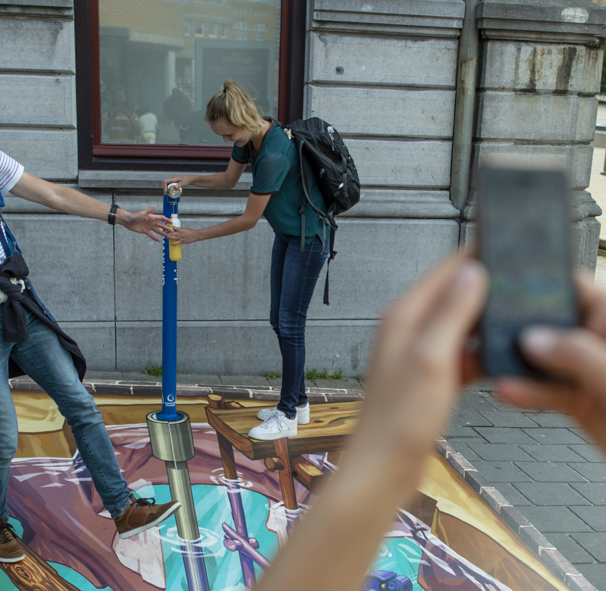 Een man en vrouw staan bij een watertappunt op de hub Groningen. Een derde persoon maakt hier een foto van.