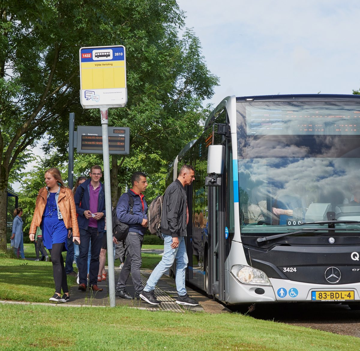 Verschillende reizigers stappen in de bus bij een bushalte.