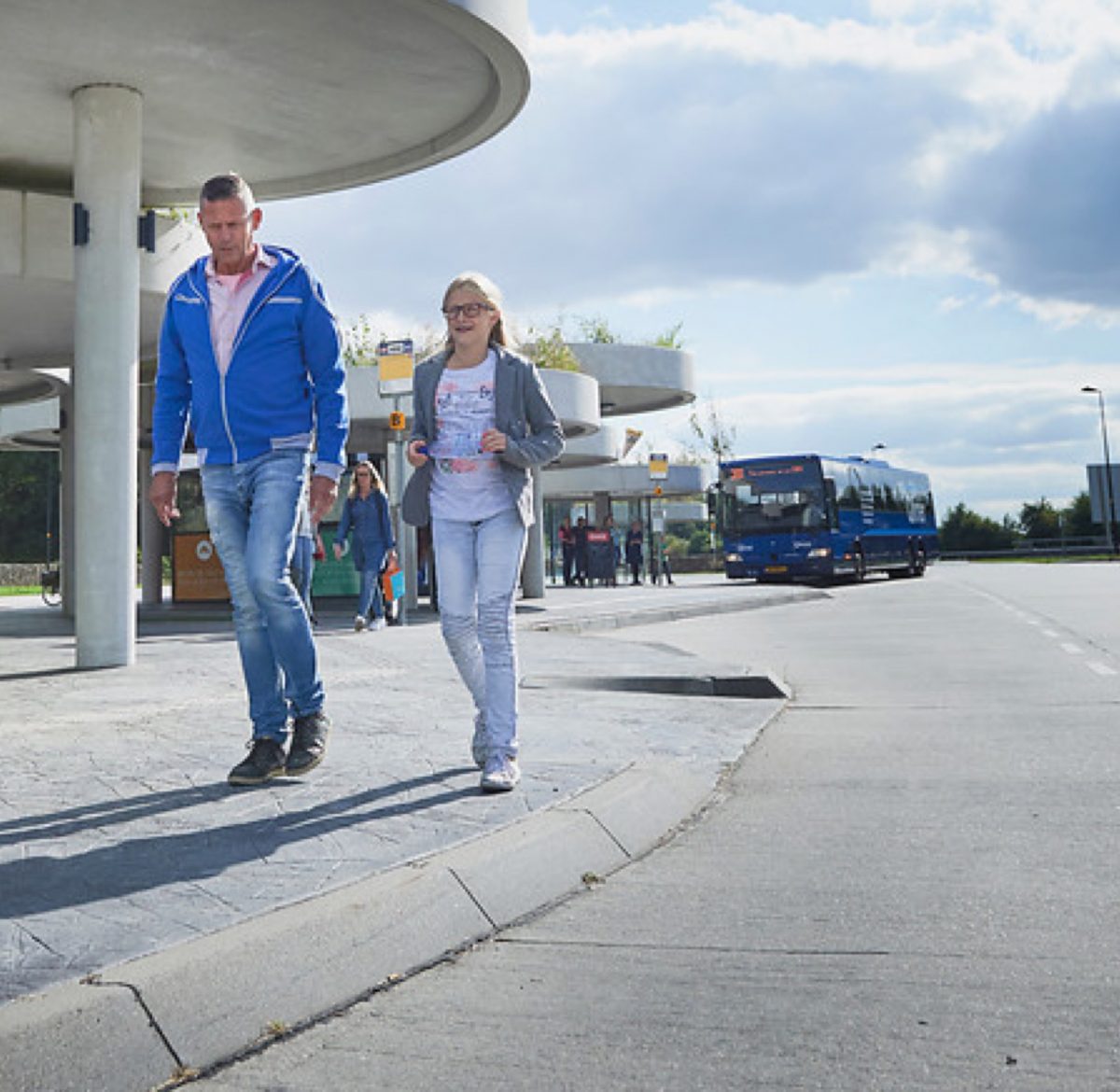 Man en kind lopen over hub in Gieten. Op achtergrond staat er een bus stil bij de bushalte.