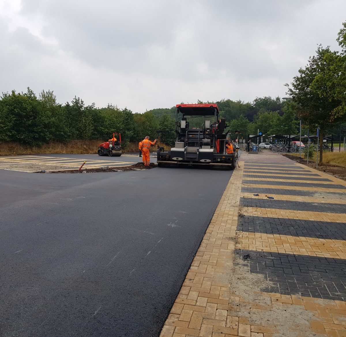 Wegwerkers brengen met een grote machine een nieuwe asfaltlaag aan op de carpoolplek van hub Westlaren.