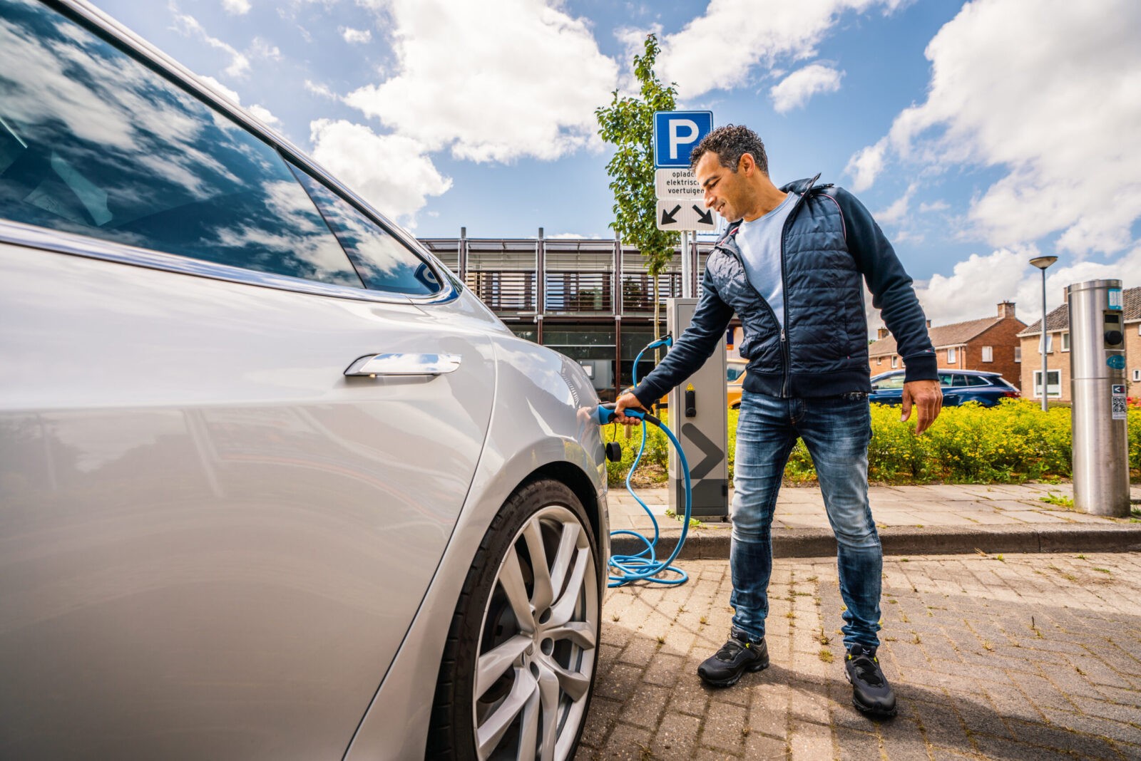 Een man gebruikt op een hub een laadpaal voor zijn elektrische auto.