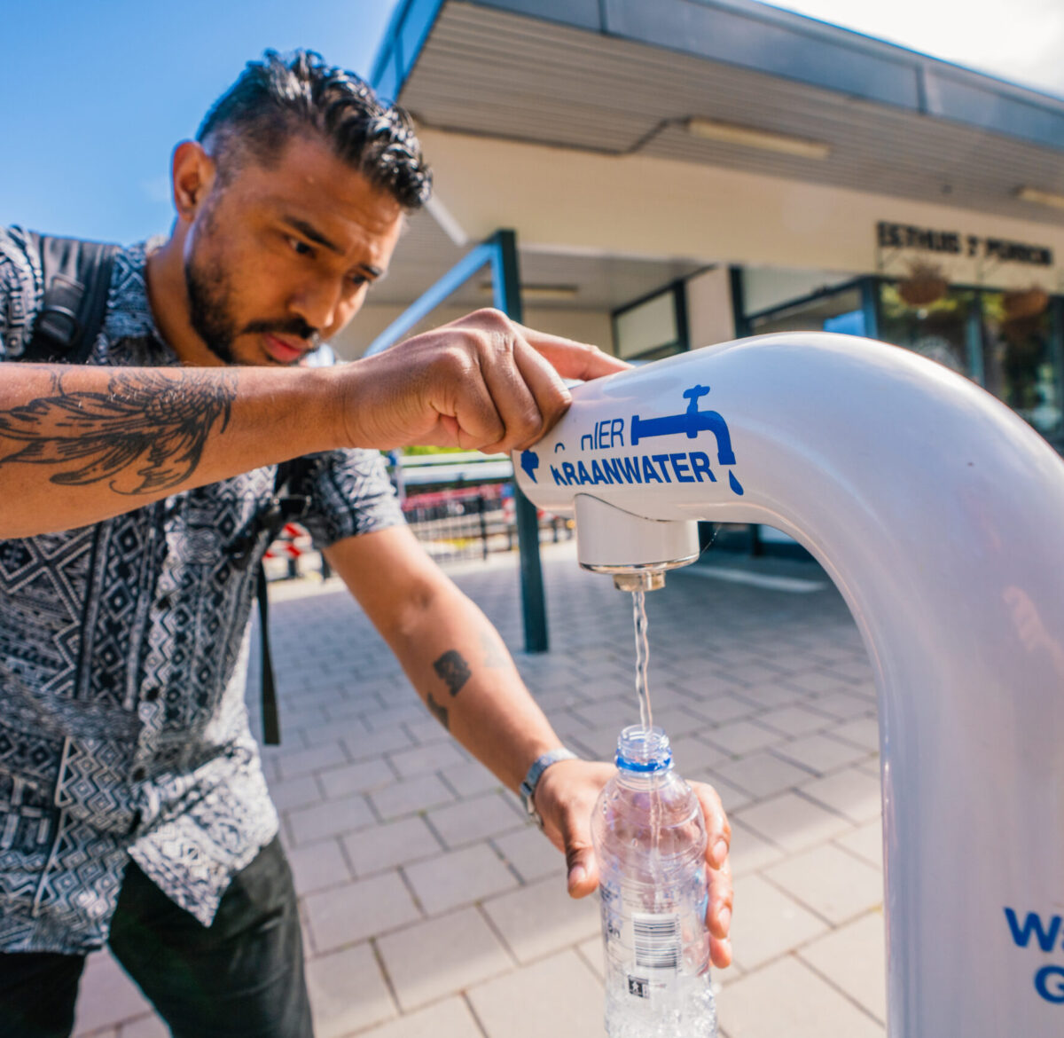 Jongen vult flesje water bij watertappunt op hub